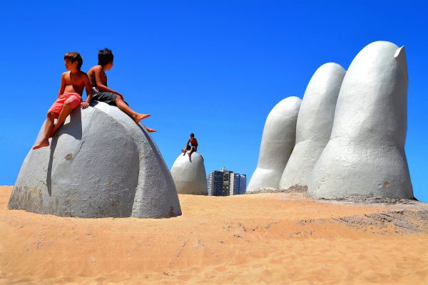 Boys Sitting on La Mano, The Hand, on Brava Beach in Punta del Este, Uruguay - Encircle Photos